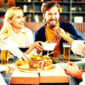 Multiethnic friends sitting at restaurant, drinking alcohol, chatting and having burgers for dinner.
